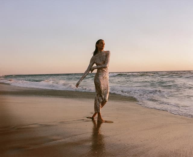 woman wearing a full length dresswalking on the beach at sunset