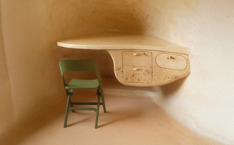 portrait of a green chair in front of an organically shaped desk in the corner of a room