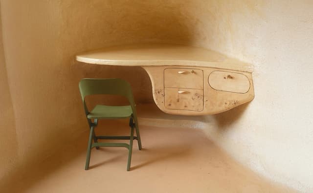 portrait of a green chair in front of an organically shaped desk in the corner of a room